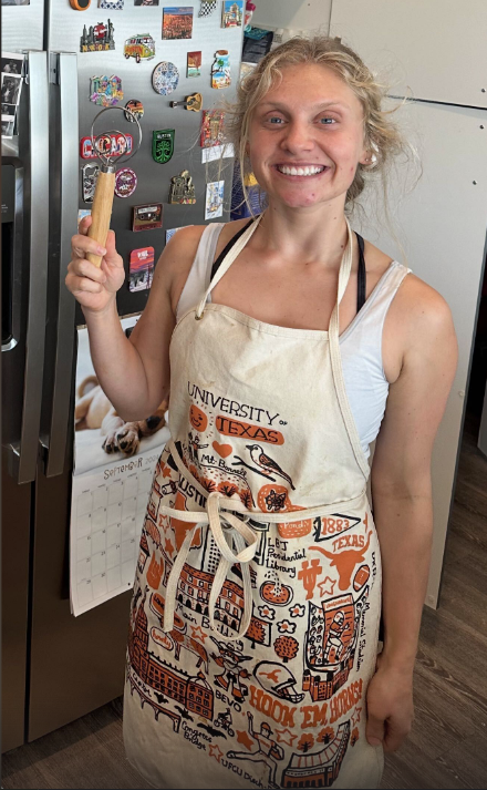 Nikki smiling in her kitchen wearing a University of Texas apron and holding a wooden spoon